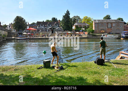 Deux jeunes adolescents garçon de pêche de la rive Tamise sur ciel bleu chaude journée d'été avec voile House pub au-delà at Wallingford Oxfordshire England UK Banque D'Images