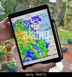 Femme hands holding ipad tablette pro alarme pluie app utilise la couleur en temps réel des données radar de précipitations carte superposant sur les temps de pluie sur la fenêtre Essex UK Banque D'Images