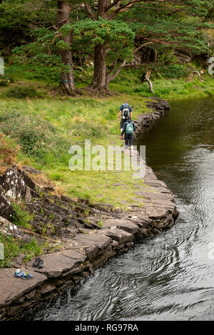 Couple de touristes routards marchant pieds nus le long de la rivière de montagne cours d'eau à la rencontre des eaux dans le parc national de Killarney, comté de Kerry, Irlande Banque D'Images