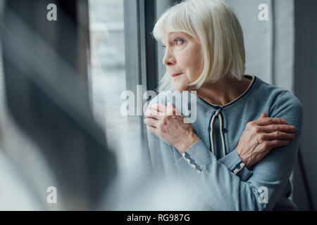 Happy woman avec mains croisées à la fenêtre grâce à à la maison Banque D'Images