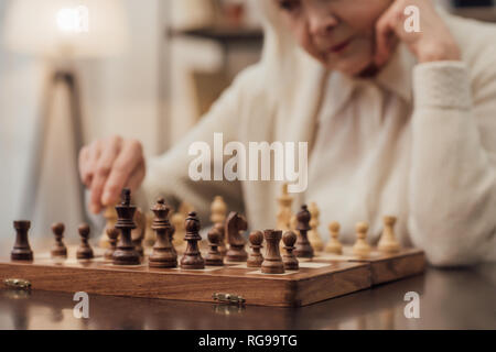 Portrait of senior woman sitting at table, soutenant le menton avec la main et jouant aux échecs à la maison Banque D'Images