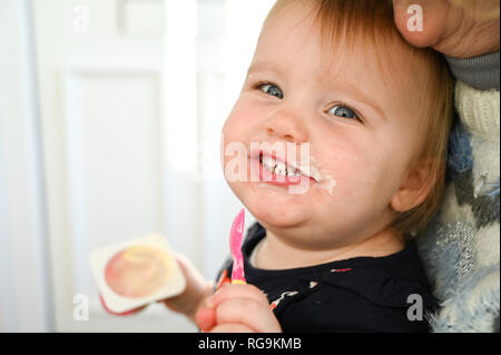 Tout-petits jeune femelle d'un peu plus de deux ans s'amusant obtenir dans un désordre de manger un yogourt photographie prise par Simon Dack Banque D'Images