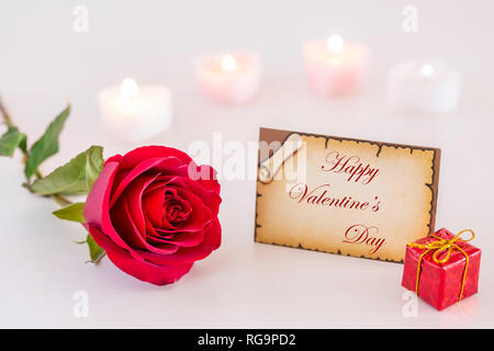 Carte de souhaits avec Happy Valentine's Day text, rose rouge, coffret-cadeau, et la lumière des bougies sur blanc Banque D'Images