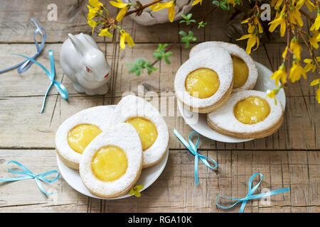 Composition de Pâques avec des cookies en forme d'œuf rempli de lait caillé de citron, lapin, bouquet de forsythia et d'arcs. Focus sélectif. Banque D'Images