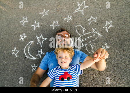 Portrait of mature man wearing hat pilote et son petit-fils gisant sur l'asphalte peint avec avion, lune et étoile Banque D'Images