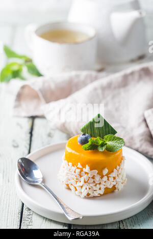 Morceau de mousse à la mangue gâteau sur une plaque sur une table en bois blanc. Banque D'Images