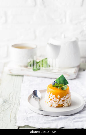 Morceau de mousse à la mangue gâteau sur une plaque sur une table en bois blanc. Banque D'Images