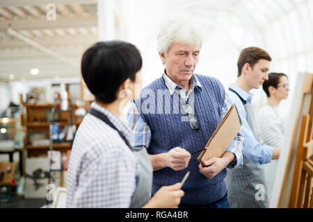 Portrait of mature art teacher helping student photo peinture sur chevalet dans la classe d'art, copy space Banque D'Images