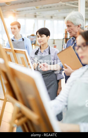 Portrait d'étudiants en art en peinture à chevalets dans la classe d'art avec jeunes adultes en les aidant à l'enseignant, copy space Banque D'Images