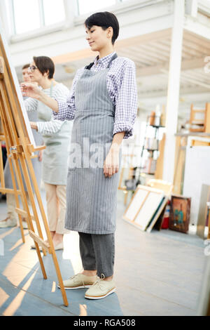 Vue latérale pleine longueur portrait de jeune femme moderne photo peinture sur chevalet dans art studio Banque D'Images