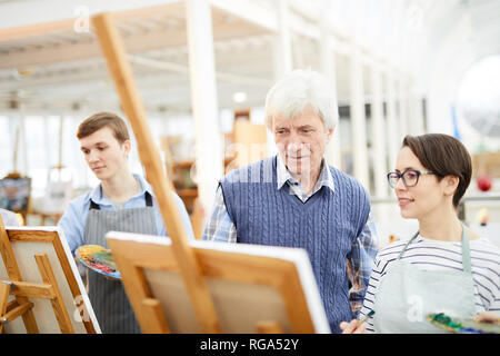 Portrait of mature professeur d'art d'aider un groupe d'étudiants photos de peinture sur des chevalets en classe d'art, copy space Banque D'Images