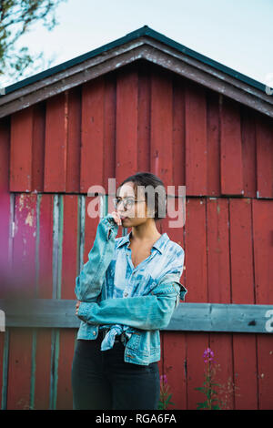 Portrait d'une jeune femme debout devant une cabane en bois rouge Banque D'Images