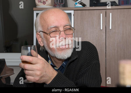 Close-up head and shoulders portrait de vieil homme chauve avec de longs cheveux gris et la barbe en noir pull tricoté fermeture éclair qui est assis avec un verre de vin Banque D'Images