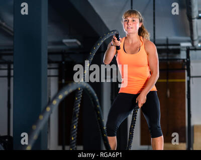 Athletic young woman exercising with ropes bataille at gym Banque D'Images
