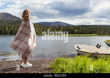 La Finlande, Laponie, femme enveloppée dans une couverture au bord de lac permanent Banque D'Images