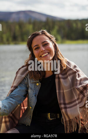 La Finlande, Laponie, portrait of smiling young woman wearing une couverture dans un bateau sur un lac Banque D'Images