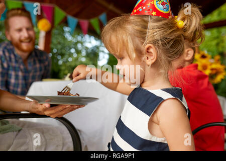 Little girl eating cake sur un anniversaire garden party Banque D'Images