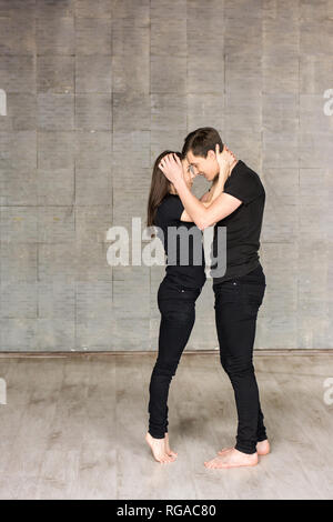 Couple de danseurs en position romantique. Portrait de beaux danseurs portant des costumes noirs hugging sur fond gris. Aimer co Banque D'Images