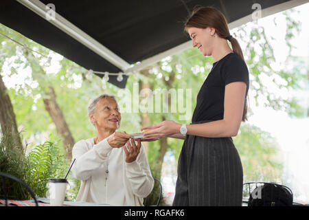 Serveuse remise plaque pour smiling senior woman at an outdoor cafe Banque D'Images