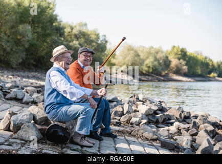 Deux vieux amis assis près du fleuve, s'amusant Banque D'Images