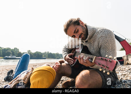 Jeune couple sympathique à jouer de la guitare à une tente au bord du fleuve Banque D'Images
