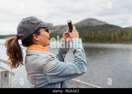 La Finlande, Laponie, happy woman on jetée à un lac en tenant un selfies Banque D'Images