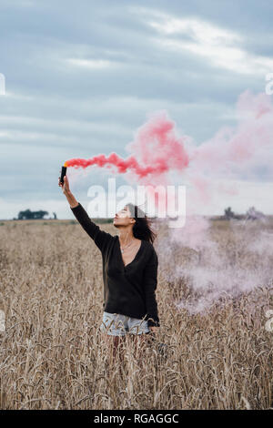 Jeune femme debout dans un champ de maïs avec torche de fumée Banque D'Images