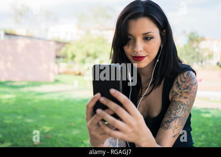 Portrait de jeune femme avec écouteurs et piercing en tenant avec smartphone selfies Banque D'Images