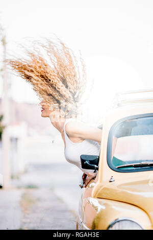 Young woman leaning out de fenêtre de voiture rejetant ses cheveux Banque D'Images