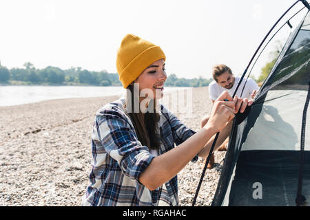 Smiling young couple mise en place d'une tente au bord du fleuve Banque D'Images