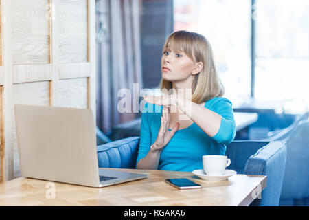 Geste de temps ! Vue de côté portrait d'attention charmante fille indépendant avec des cheveux blonds en blouse bleue sont assis dans un café et faire appel vidéo Banque D'Images