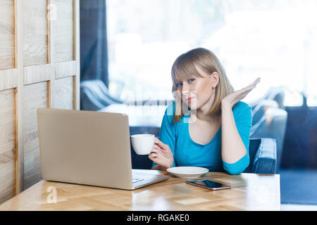 Portrait de la belle jeune fille blonde réfléchie avec Bob coupe de cheveux en blouse bleue sont assis dans un café et parler avec ami thoung sur webcame Banque D'Images