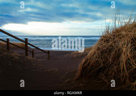 Un escalier en bois mène à une plage de sable volcanique noir sur les rives de l'océan Atlantique en Islande Banque D'Images