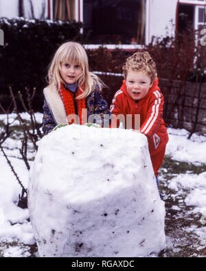 Deux jeunes enfants, une fille et un garçon, roulant une grosse boule de neige pour faire une base pour un bonhomme de neige. Banque D'Images