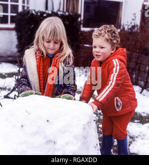 Deux jeunes enfants, une fille et un garçon, roulant une grosse boule de neige pour faire une base pour un bonhomme de neige. Banque D'Images