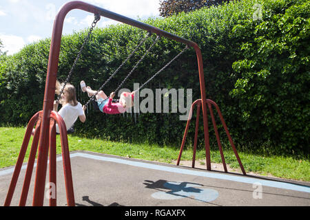 Deux filles caucase jouant sur des balançoires dans un parc d'une aire de jeux Banque D'Images