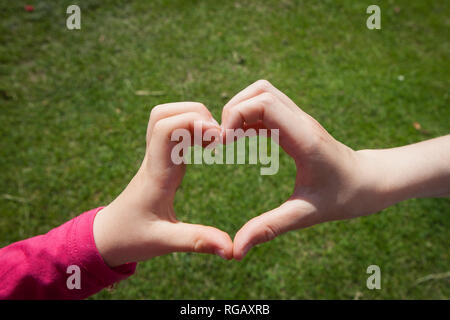 Les mains des enfants faisant un coeur d'amour signe au-dessus de l'herbe Banque D'Images