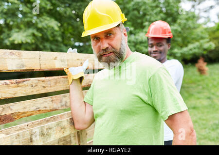 Construction Worker with hard hat porte une palette de transport avec l'aide d'un collègue Banque D'Images