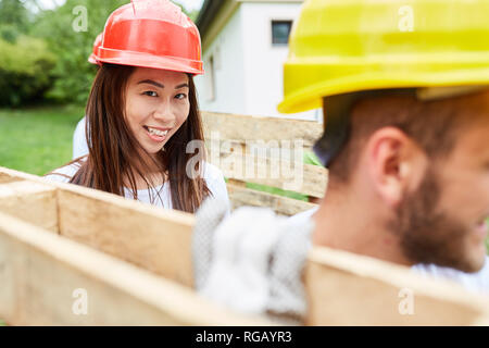 Jeune femme d'apprenti-travailleur de la construction porte palettes, avec l'aide d'un collègue Banque D'Images