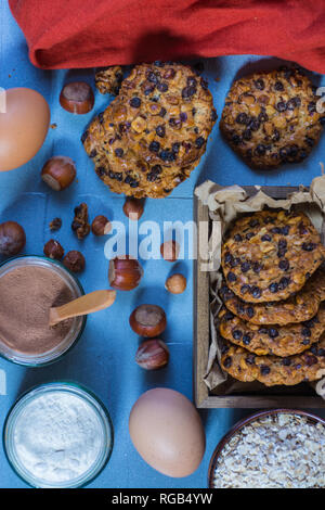 Avena cookies aux noisettes et pépites de chocolat, une boîte avec des cookies, deux œufs, deux bols avec du chocolat et de la farine, un bol et un chiffon avena Banque D'Images