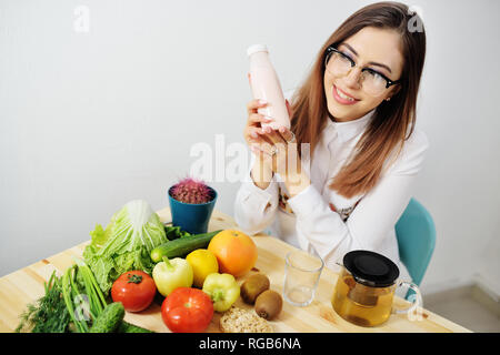 Jeune fille mignonne avec du yogourt ou kéfir holding verres dans une bouteille sur l'arrière-plan d'une table avec beaucoup de légumes Banque D'Images