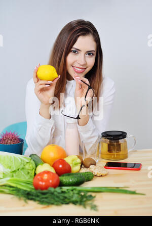 Jeune fille mignonne avec les citrons mûrs holding lunettes sur l'arrière-plan d'une table avec beaucoup de légumes. Banque D'Images