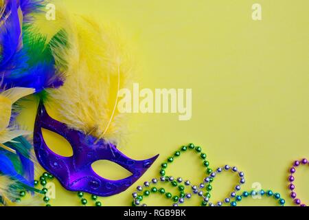 Masque Mardi Gras entouré d'un boa et plumes colorés colliers de perles sur un fond jaune. Banque D'Images