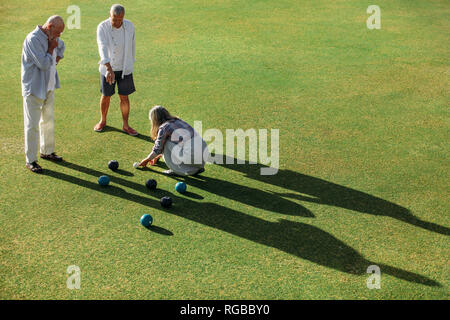 Senior woman mesurant la distance entre les boules et la jack alors que ses amis masculins. Des personnalités de contrôler la distance entre les b Banque D'Images