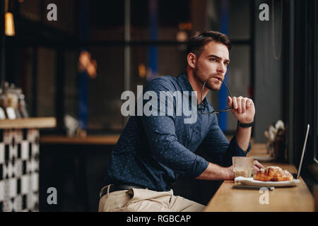 Entrepreneur indépendant assis dans un restaurant travaillant sur ordinateur portable et pensant profondément. homme d'affaires travaillant sur ordinateur portable assis dans un restaurant avec de la nourriture Banque D'Images