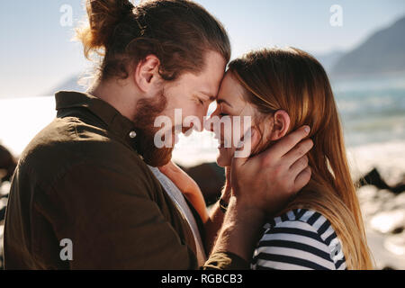 Vue de côté de l'homme et la femme se tient à proximité de toucher leur front à une plage. Couple romantique bénéficiant d'une journée sur la plage. Banque D'Images