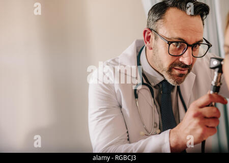 Spécialiste en ORL à la recherche dans l'oreille du patient avec un otoscope à sa clinique. Doctor examining patient's ear avec instrument. Banque D'Images