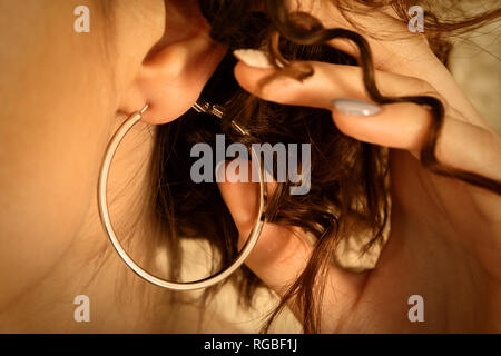 Belle femme avec de grandes boucles d'oreille et la main dans les cheveux en boucle Banque D'Images