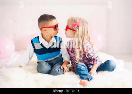 Portrait de deux professionnels white Caucasian mignon drôle adorables enfants portant des lunettes en forme de coeur. Garçon et fille essayant d'embrasser l'autre. L'amour, friendsh Banque D'Images