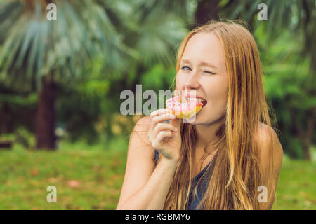 Portrait of a young woman eating a donut contre un arrière-plan de l'usine Banque D'Images